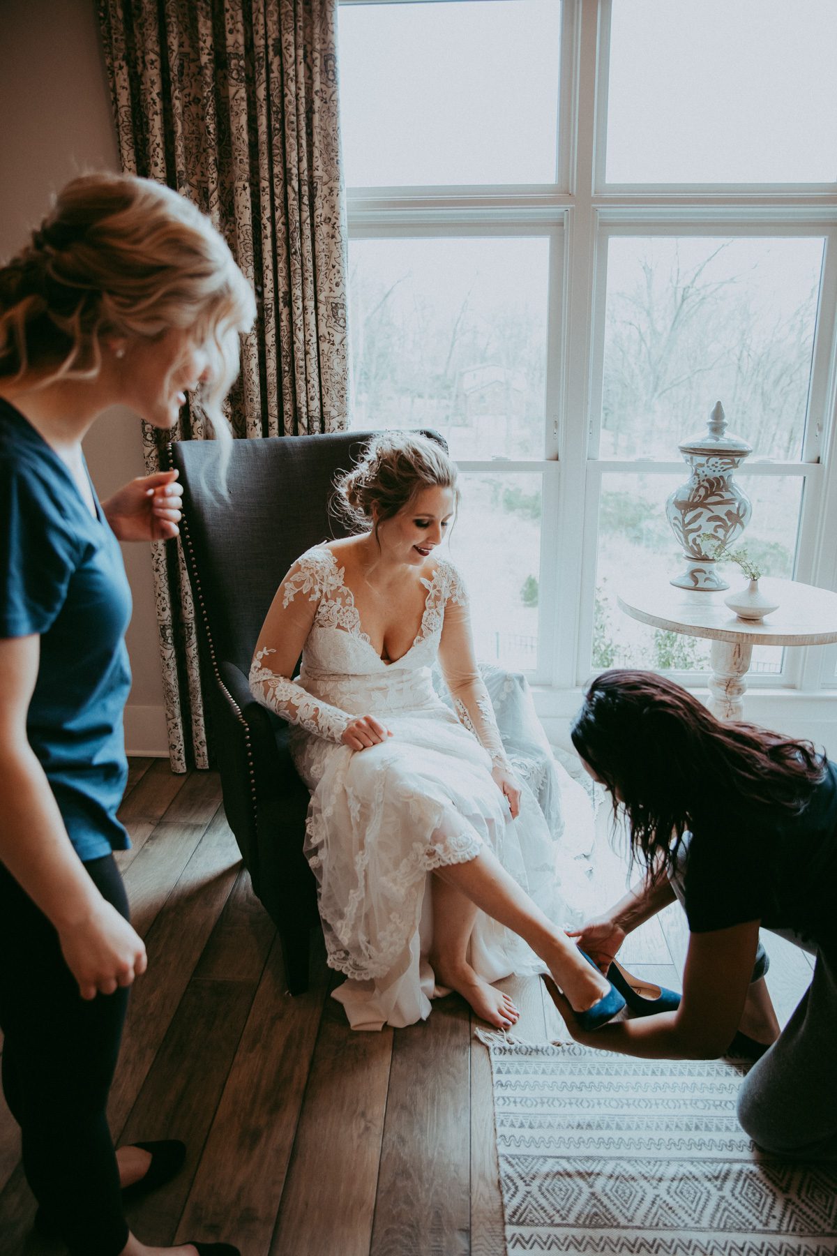 Bride gets help putting on blue shoes on her wedding day 