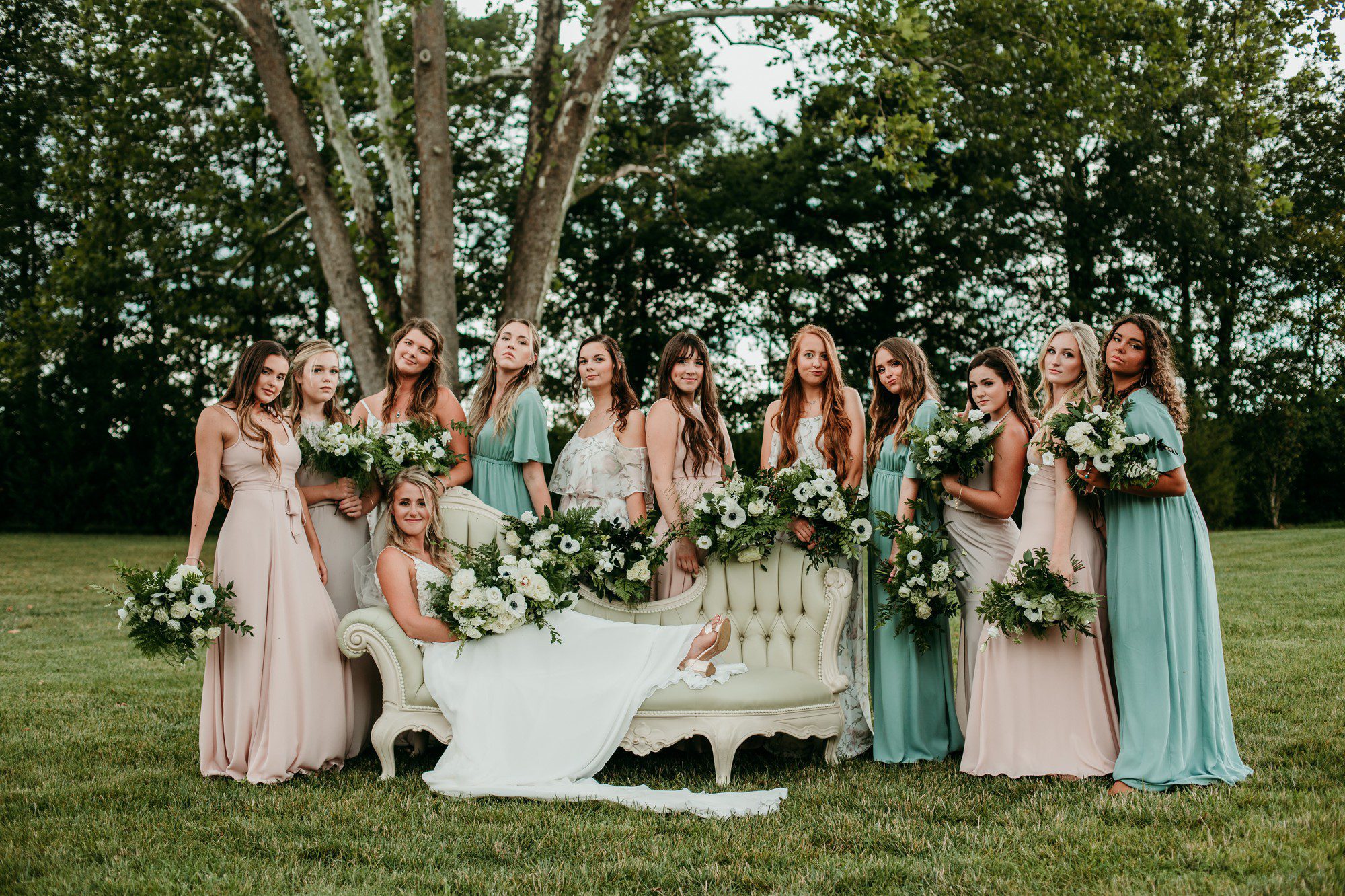 Mixed bridesmaid dresses with blush pink, aqua and floral prints and bride on sofa